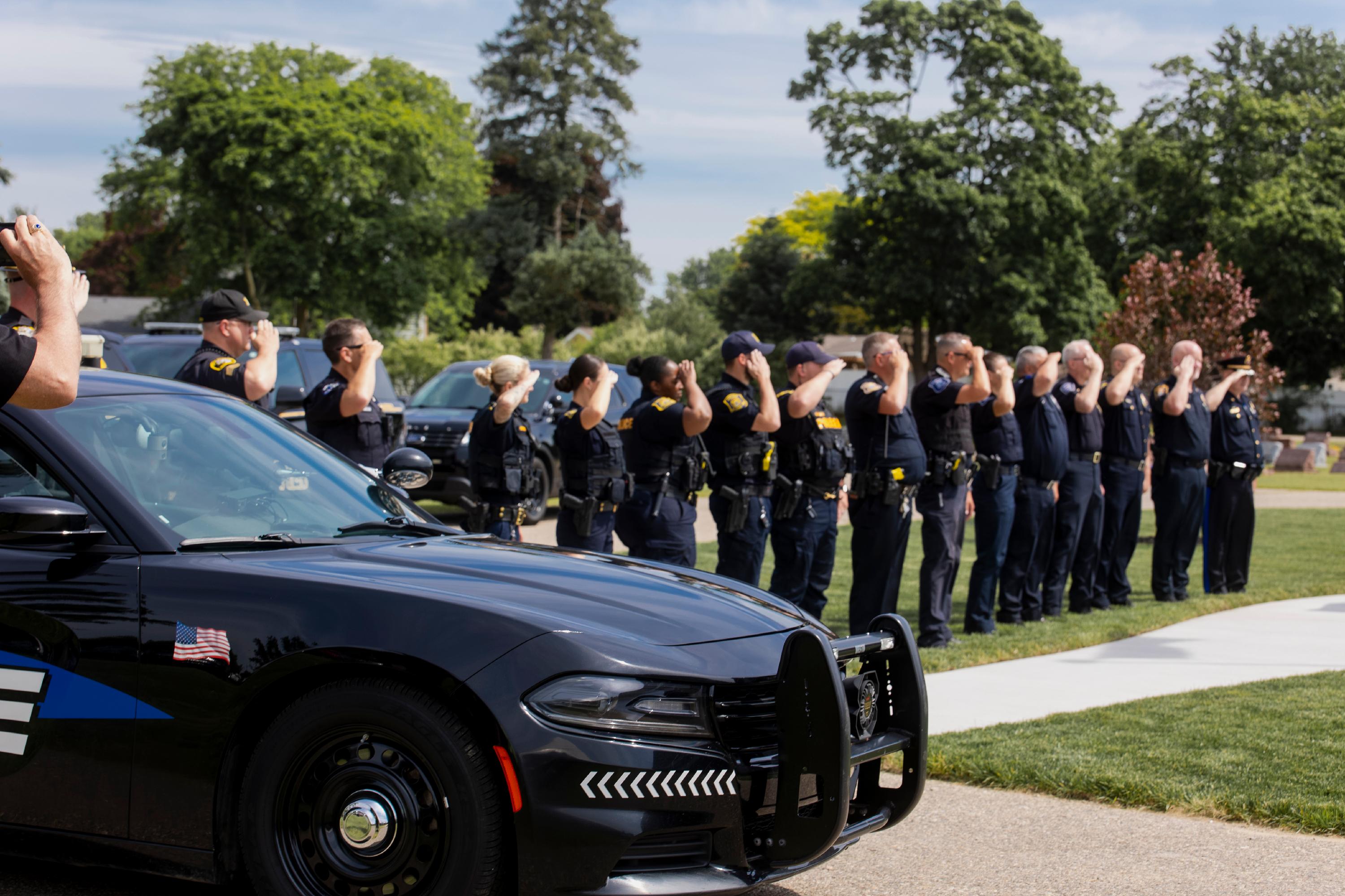 A group of police officers stands in front of a police car, dressed in uniforms and engaged in conversation